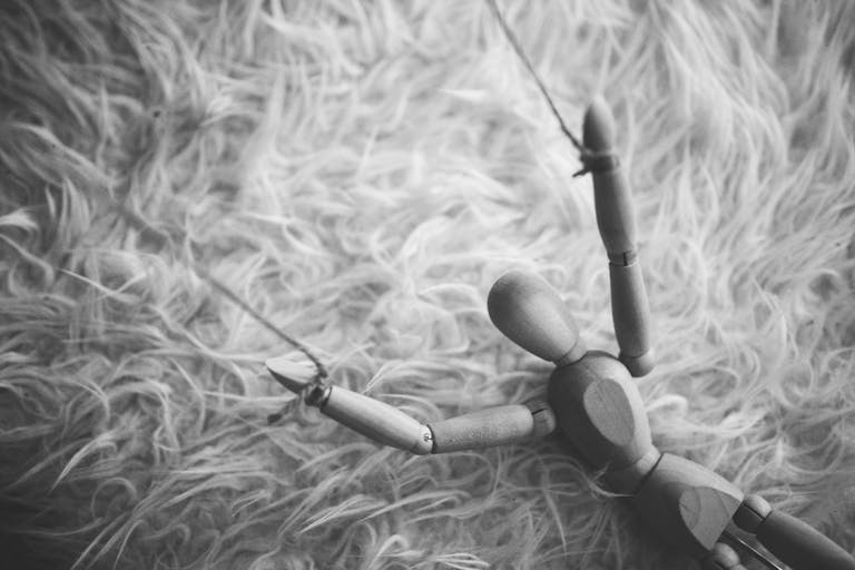 Black and white image of a wooden puppet laying on a furry surface, evoking a dramatic and artistic mood.