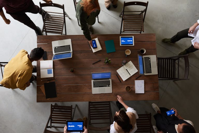 Overhead view of a team brainstorming around a table with laptops and notebooks in an office setting.