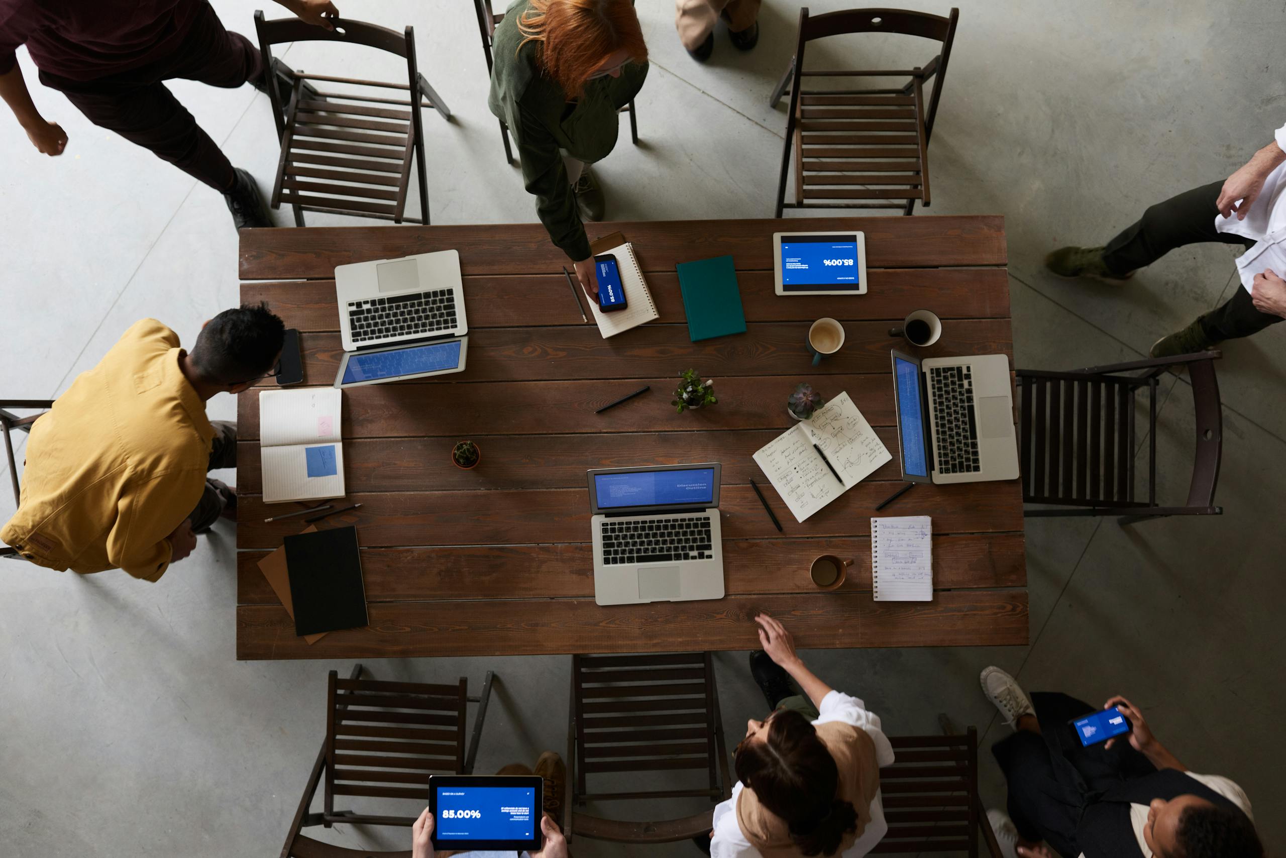 Overhead view of a team brainstorming around a table with laptops and notebooks in an office setting.