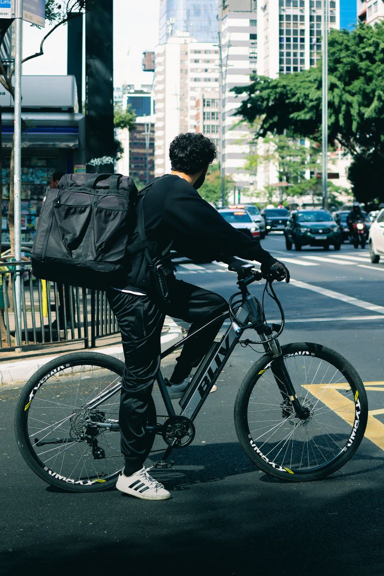 Bicycle delivery rider waiting at a busy city street intersection.