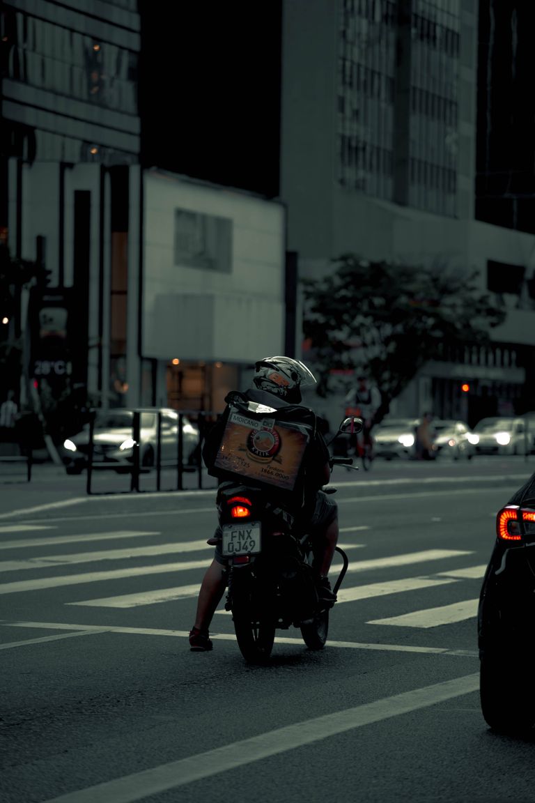 A delivery person on a motor scooter navigates city streets at twilight.
