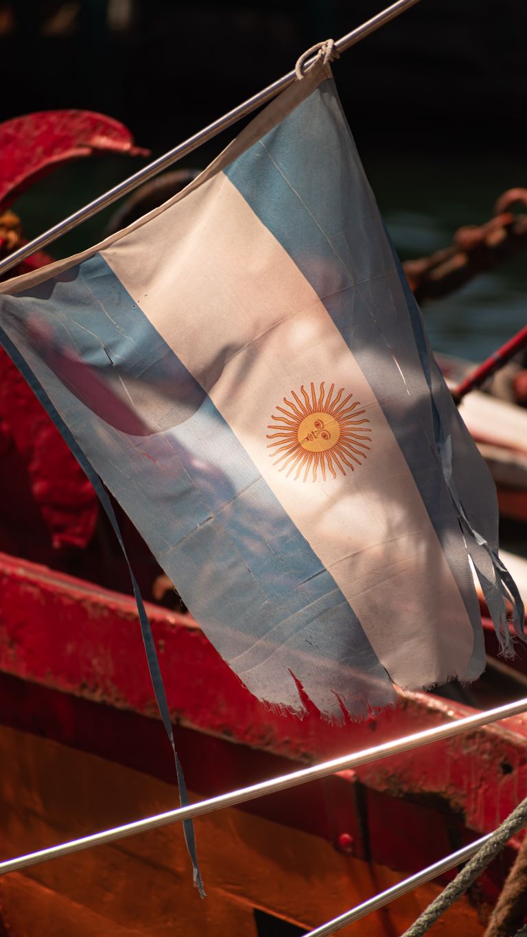 Close-up of a worn Argentine flag fluttering on a vintage ship under sunlight.